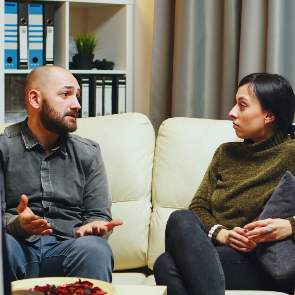 Man-with-neutral-expression-on-sofa-talking-to-a-woman-aspect-ratio-500-500
