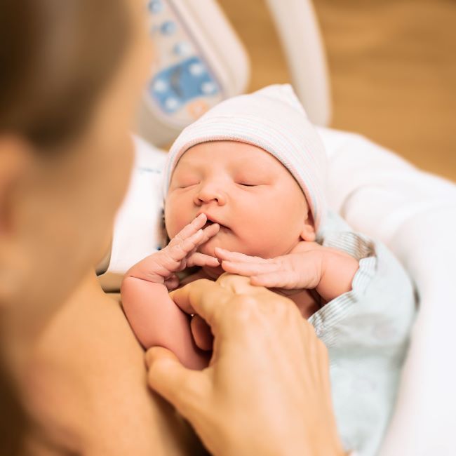Close up of a newborn baby, with woman's hand and face just out of shot