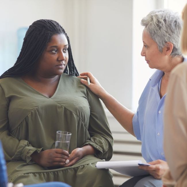 A woman in a counselling session with the therapist placing a comforting hand on her shoulder