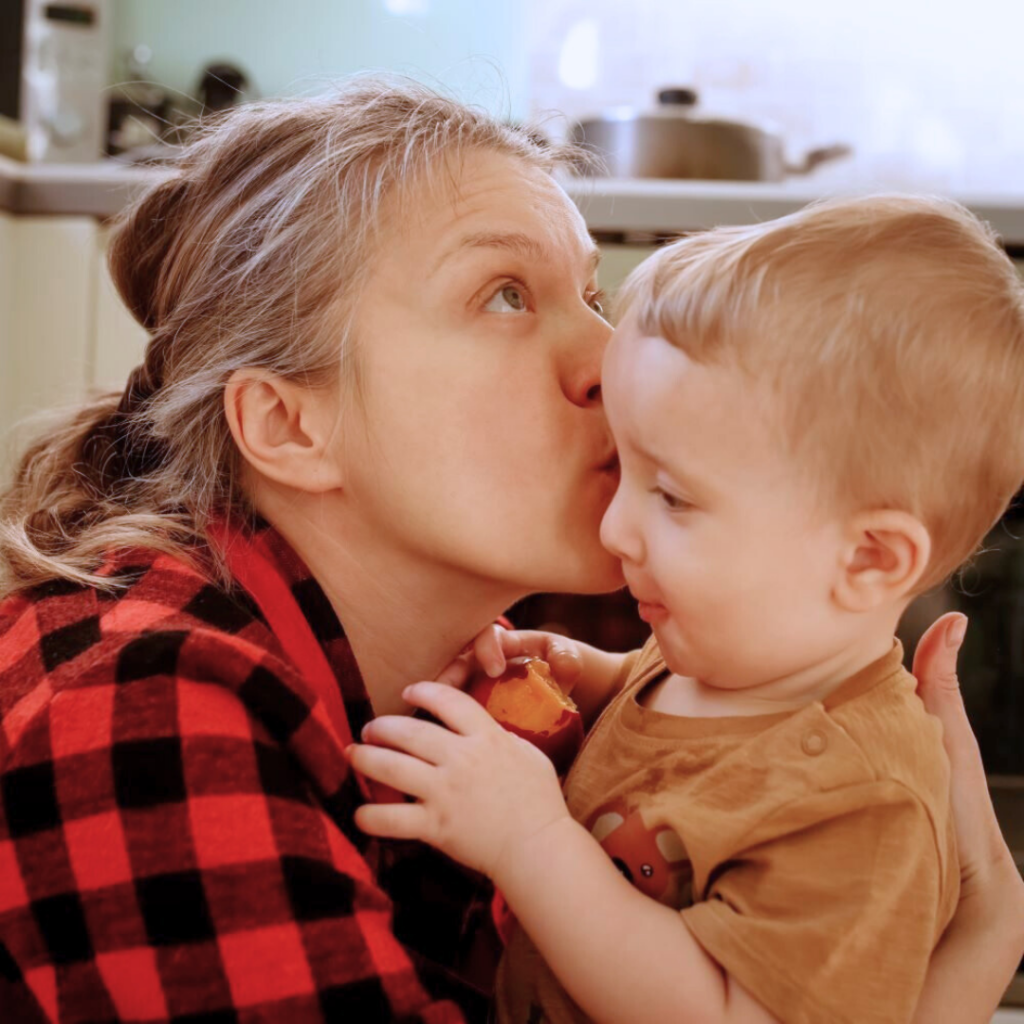 In their kitchen, a blonde mum looks up as she kisses her baby son on the forehead.